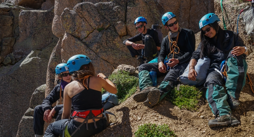 A group of people wearing safety gear rest on rocks.